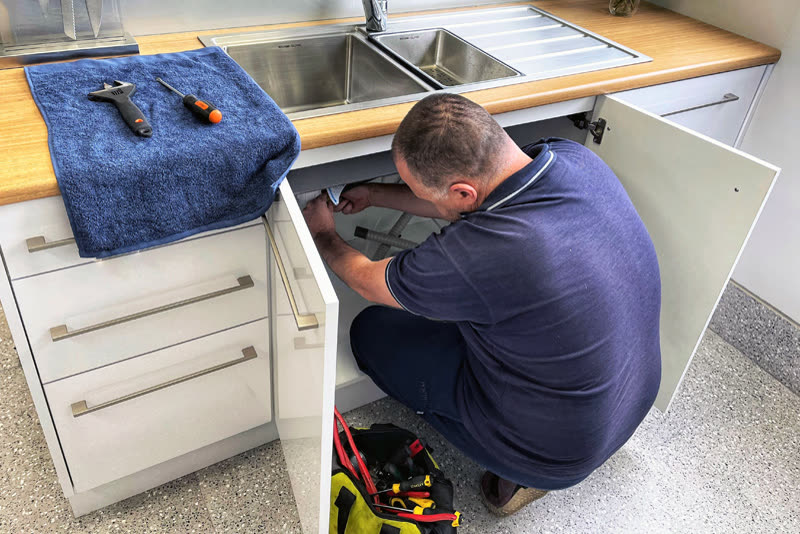 Plumber repairing plumbing pipes under a kitchen sink