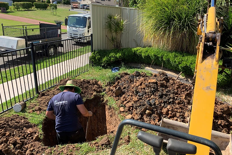 Plumber working in a newly excavated trench beside a Leonay Plumbing truck
